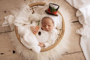Overhead view of baby lying in white linen and fur on round wooden surface in neutral tones.