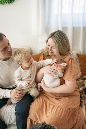 Family shares tender moments together on a white couch, wearing peach and white clothing in a bright room.