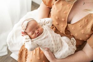 A parent gently cradles a newborn baby wrapped in soft white fabric against a neutral background.