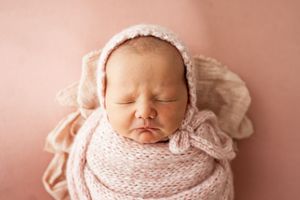 Peaceful newborn baby swaddled in soft pink fabric against a rosy backdrop.