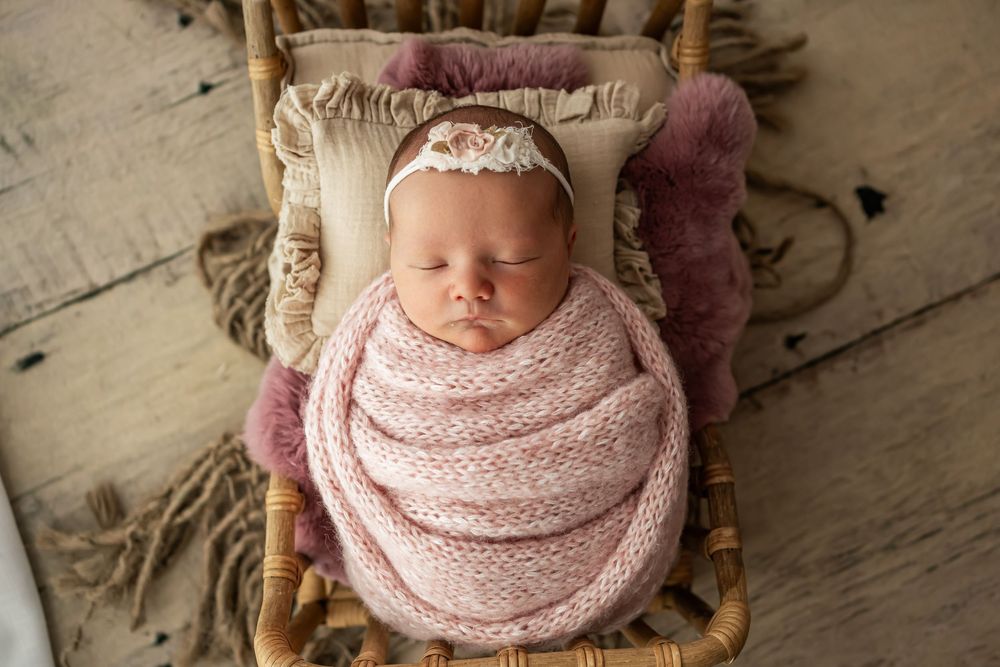 A sleeping newborn wrapped in soft pink fabric lying on a rustic wooden backdrop.