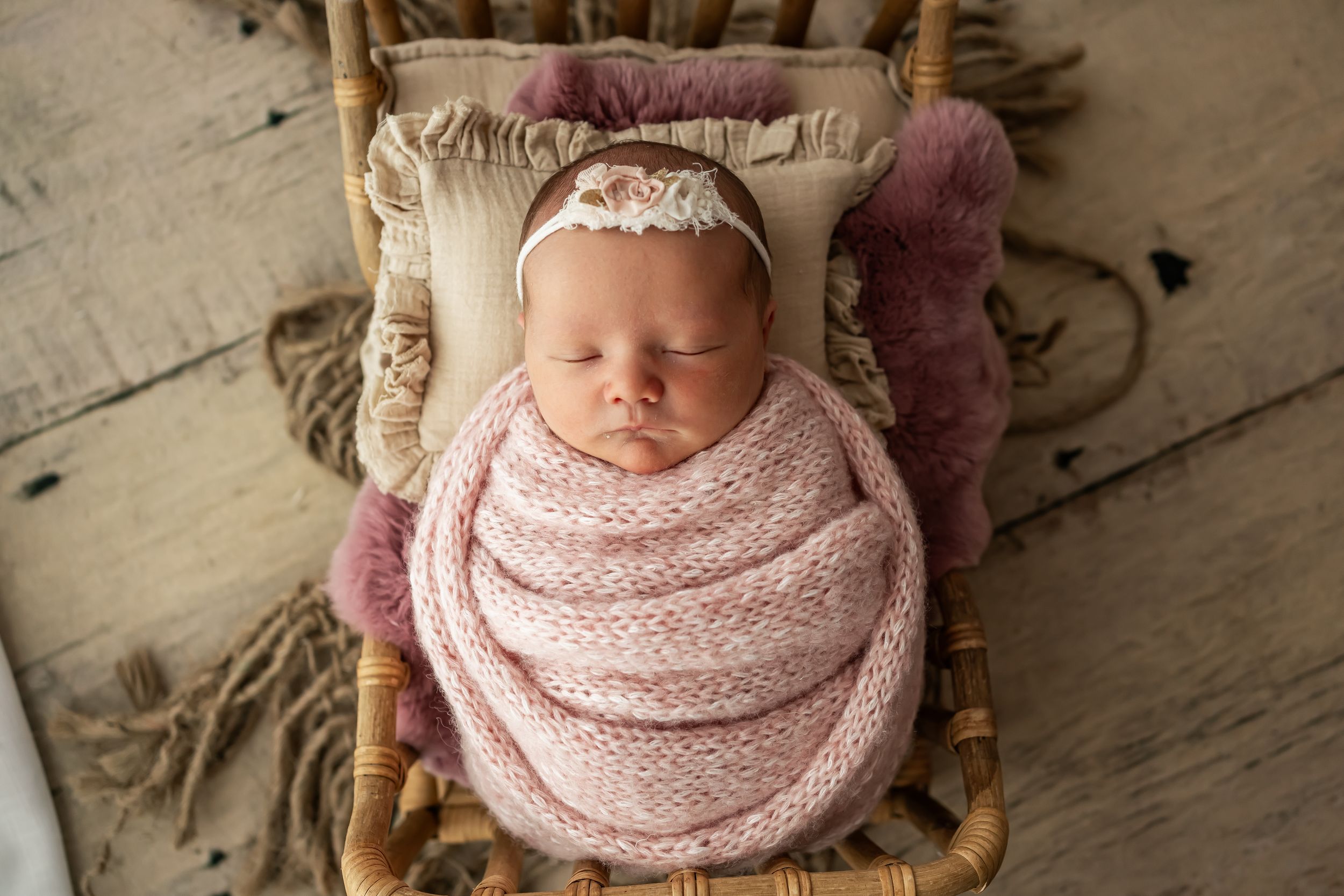 A sleeping newborn wrapped in soft pink fabric lying on a rustic wooden backdrop.