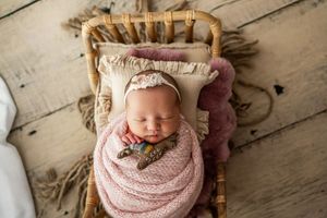 Sleeping newborn wrapped in blush pink knit wrap on rustic wooden floor.
