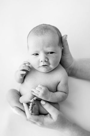 Black and white series of artistic newborn baby portraits showing gentle cradling in adult hands.