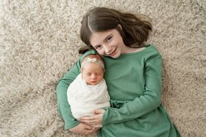 A tender moment between parent and baby wearing white as they lay together on a soft gray carpet.