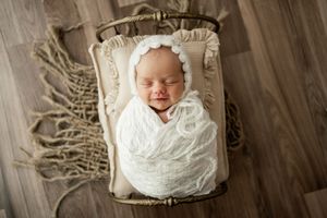 Newborn baby photography series showing peaceful sleeping infant wrapped in white blanket on wooden backdrop.
