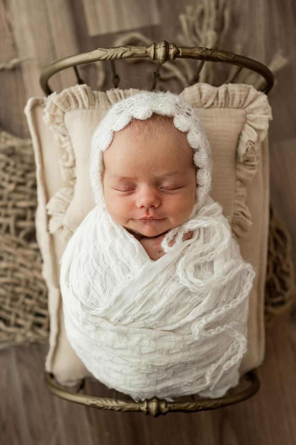A sleeping newborn baby swaddled in soft white fabric lies peacefully in a rustic wooden basket.