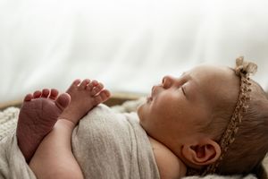 A newborn baby sleeping peacefully in a cream-colored wrap during a professional photo session.
