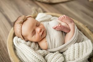 Peaceful newborn baby sleeping in wooden bowl wrapped in soft white fabric and knitted blanket.