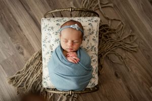 Collage of newborn photography showing six artistic poses with soft blue wrapping on rustic wooden floor.