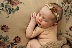 Sleeping newborn baby wearing a delicate floral headband against floral backdrop.