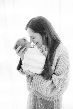 A tender black and white portrait of a woman in a knit sweater sharing a joyful moment with a newborn baby.