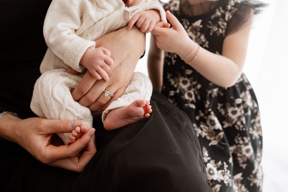 Close up shots of hands cradling a newborn baby against a floral patterned background.