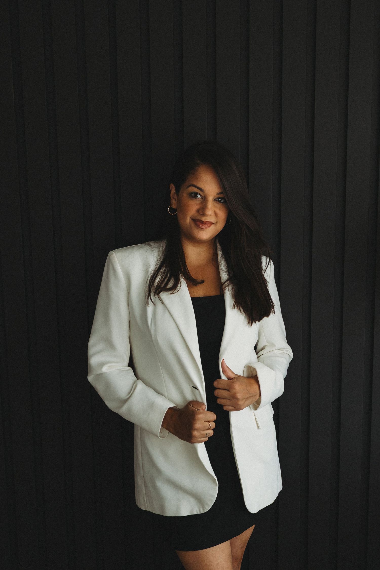 Professional fashion photography session against a dark background with white blazer.