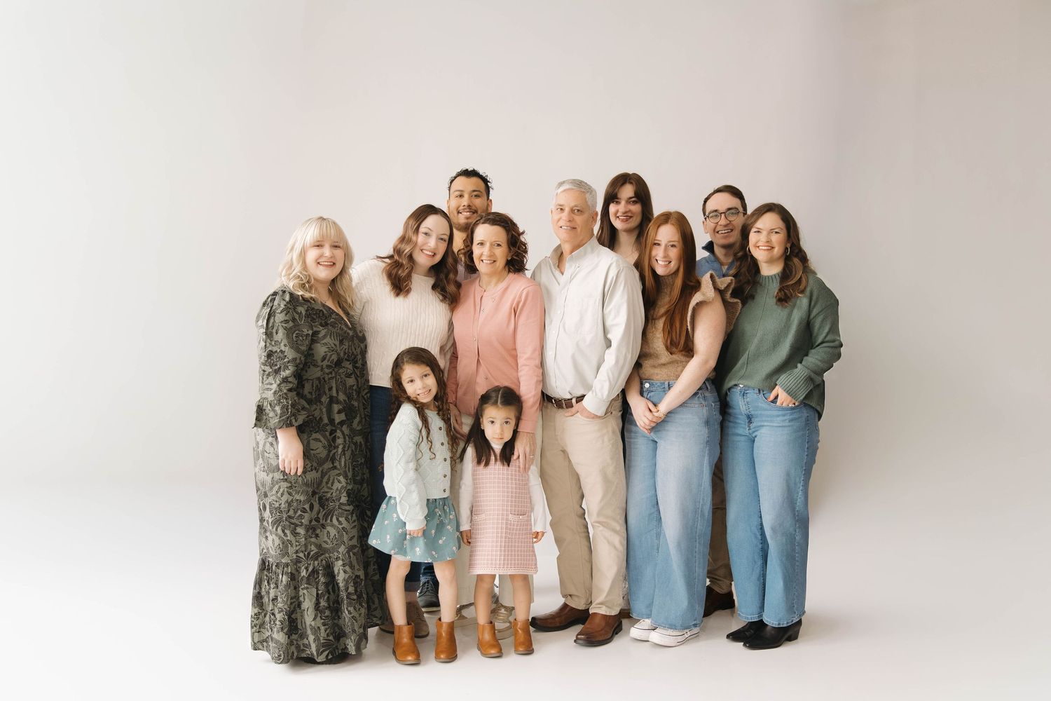 A group of people wearing casual clothing poses together against a neutral studio backdrop for a family portrait.