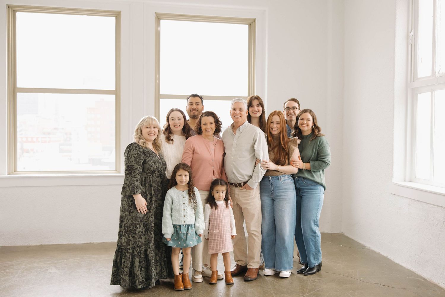 A group of people in casual attire stand together in a bright white room with large windows.