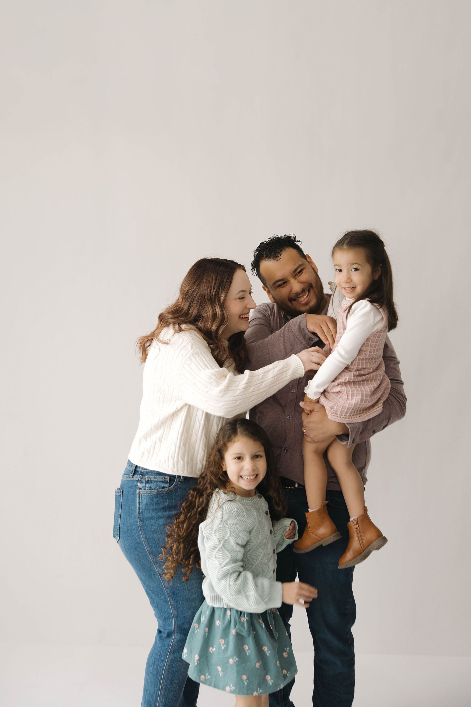 A family shares tender moments in a series of four candid photos against a light gray studio backdrop.