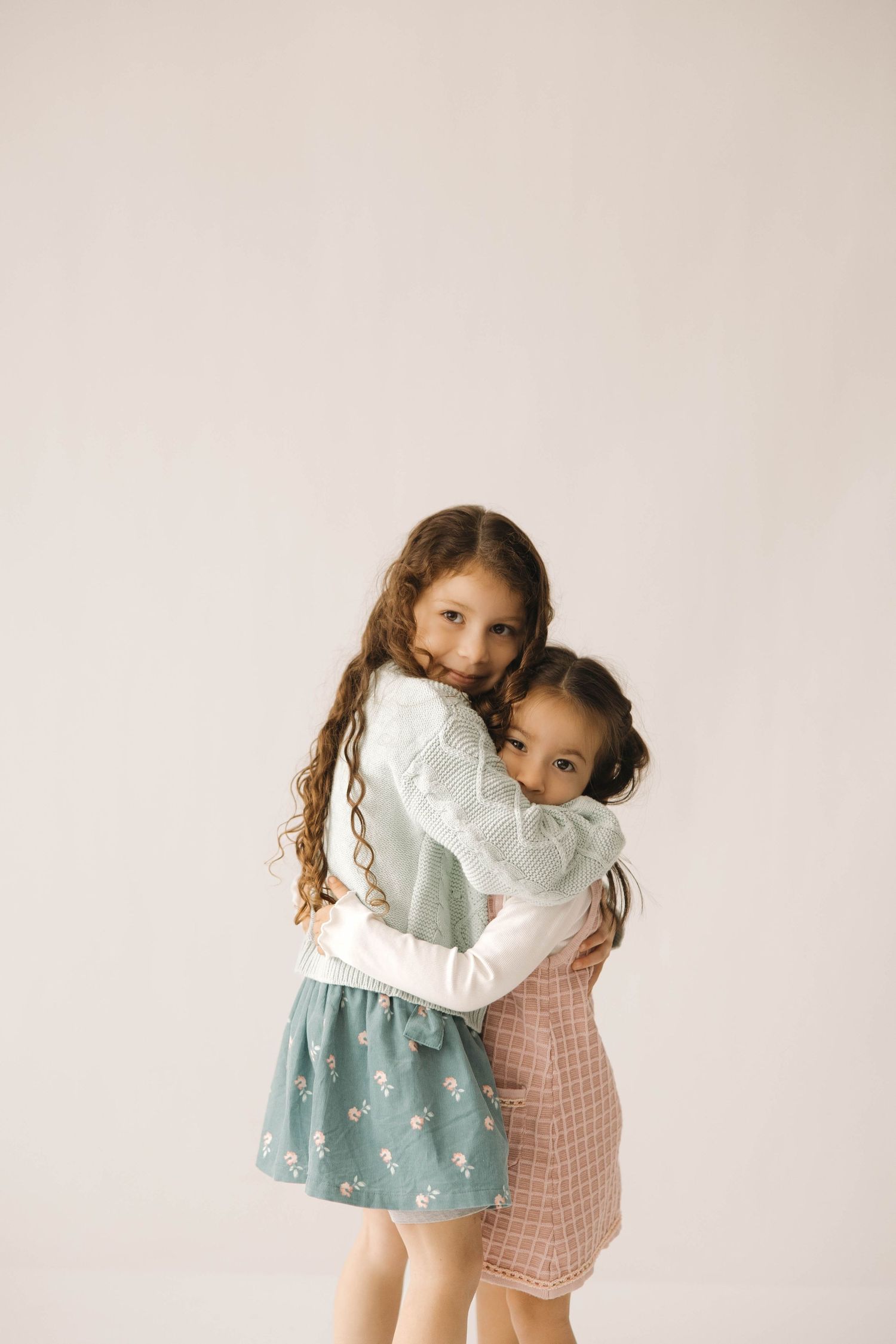 Two young children in pastel dresses share a sweet hug in a series of candid photos against a light background.