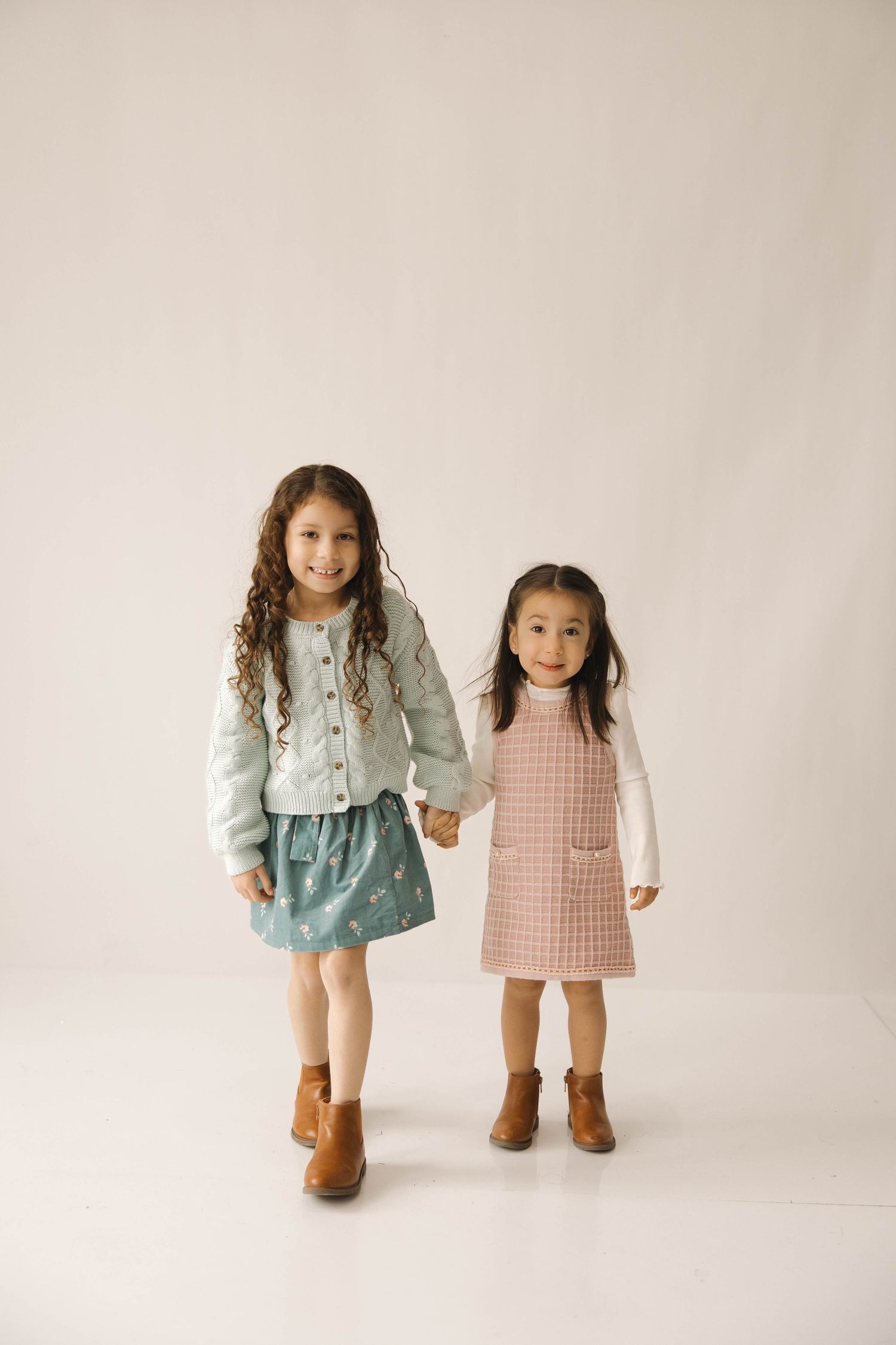 Two children wearing coordinating outfits with denim and pink dresses pose together against a white backdrop.