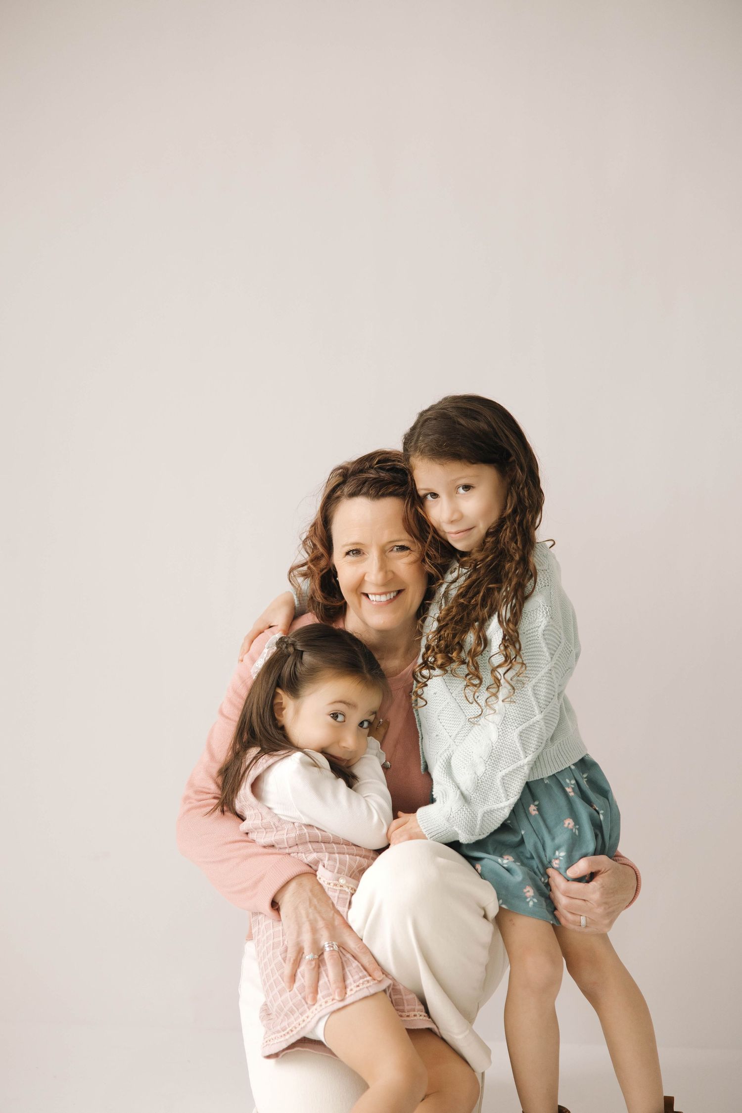 Family portrait showing tender embrace between parent and children against neutral background.