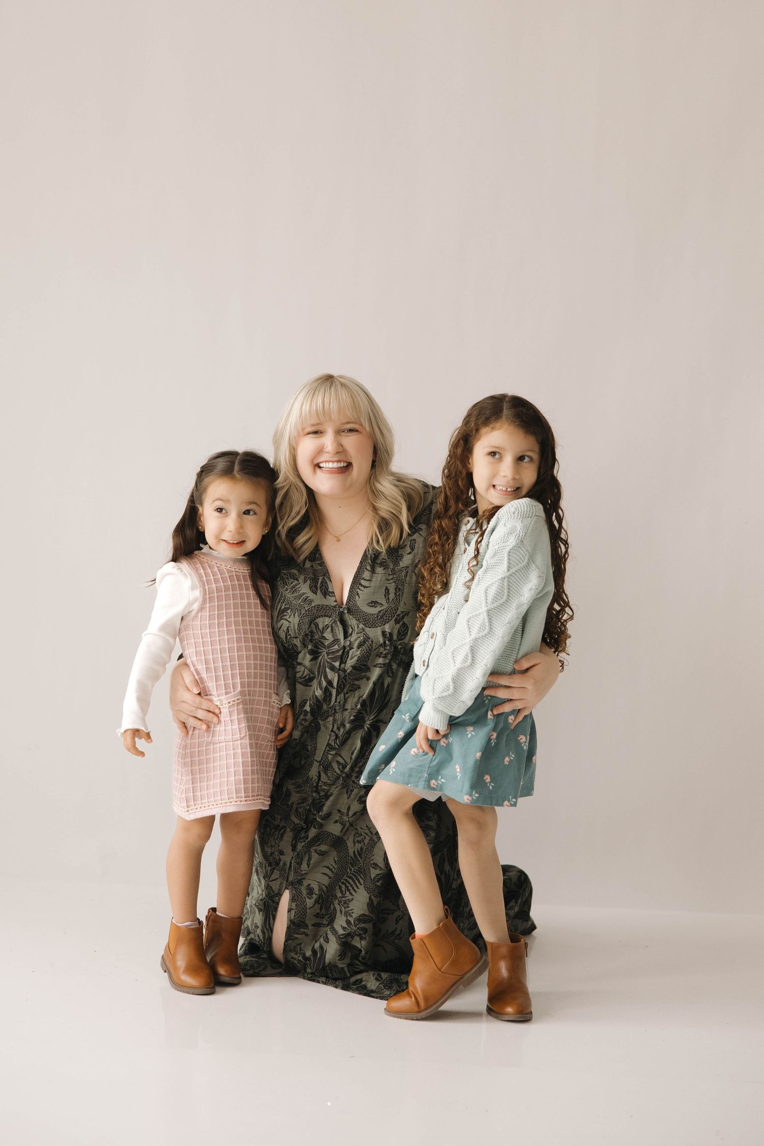 Children pose together wearing vintage-style dresses and boots against a neutral backdrop.