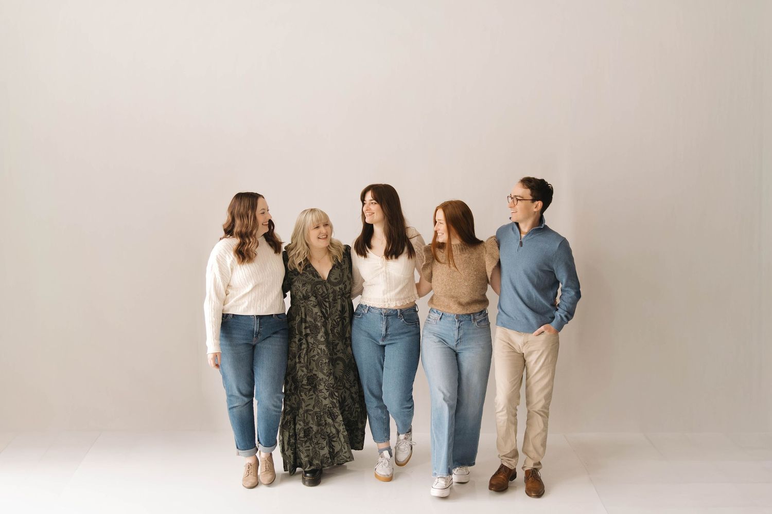 A group of people wearing casual denim and neutral tones stand together against a white background.