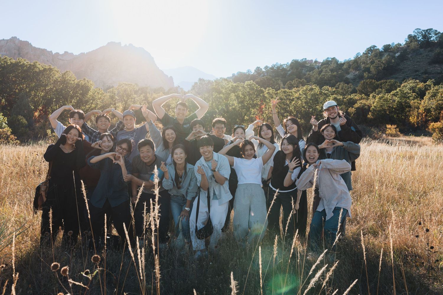 Group of people celebrating outdoors at sunset in a golden field with mountains in background.