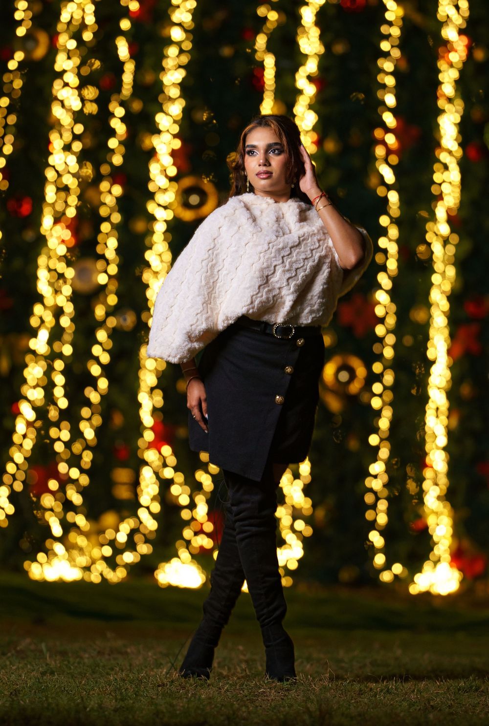 Fashion portrait with white knit sweater and black skirt against a backdrop of glowing string lights at night.