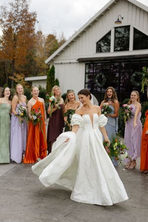 Bride twirls in white gown surrounded by bridesmaids in orange and purple dresses.