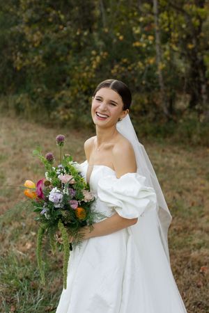 Bride holds colorful autumn bouquet in elegant white wedding dress with flowing veil.