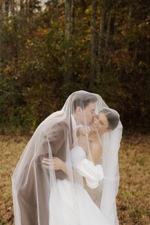 Romantic wedding couple shares intimate moment under flowing veil in autumn setting.