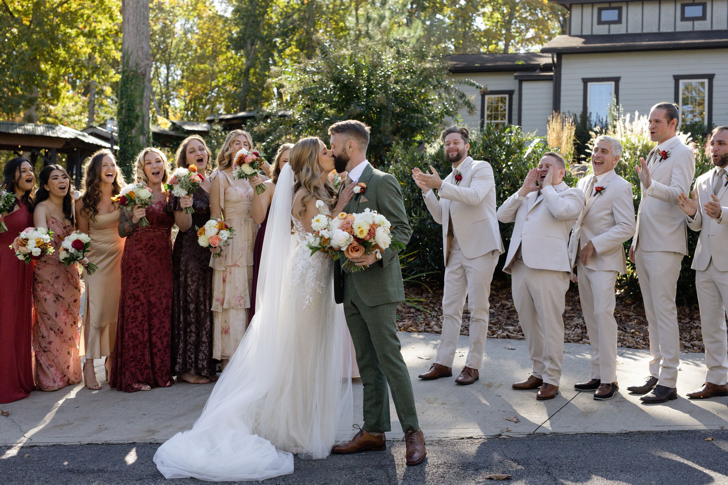 Wedding party in white and burgundy attire poses together outdoors.