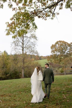 Couple takes romantic wedding photos on a grassy hillside with autumn trees in the background.