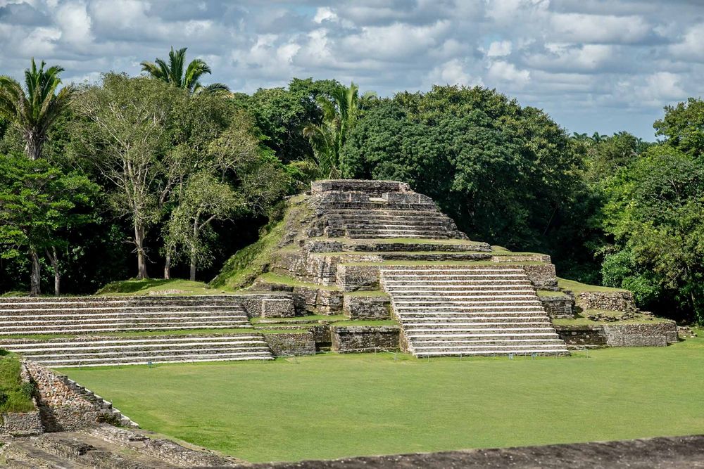 Panoramic view of Mayan temple ruins with stepped pyramids against blue sky with white clouds.