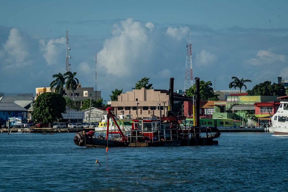 A panoramic view of waterfront homes and boats along a tropical coastline with blue skies and palm trees.