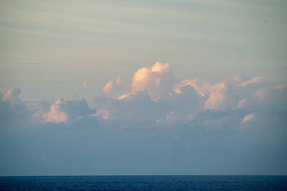 Pink-tinted clouds float above a calm ocean horizon during golden hour.