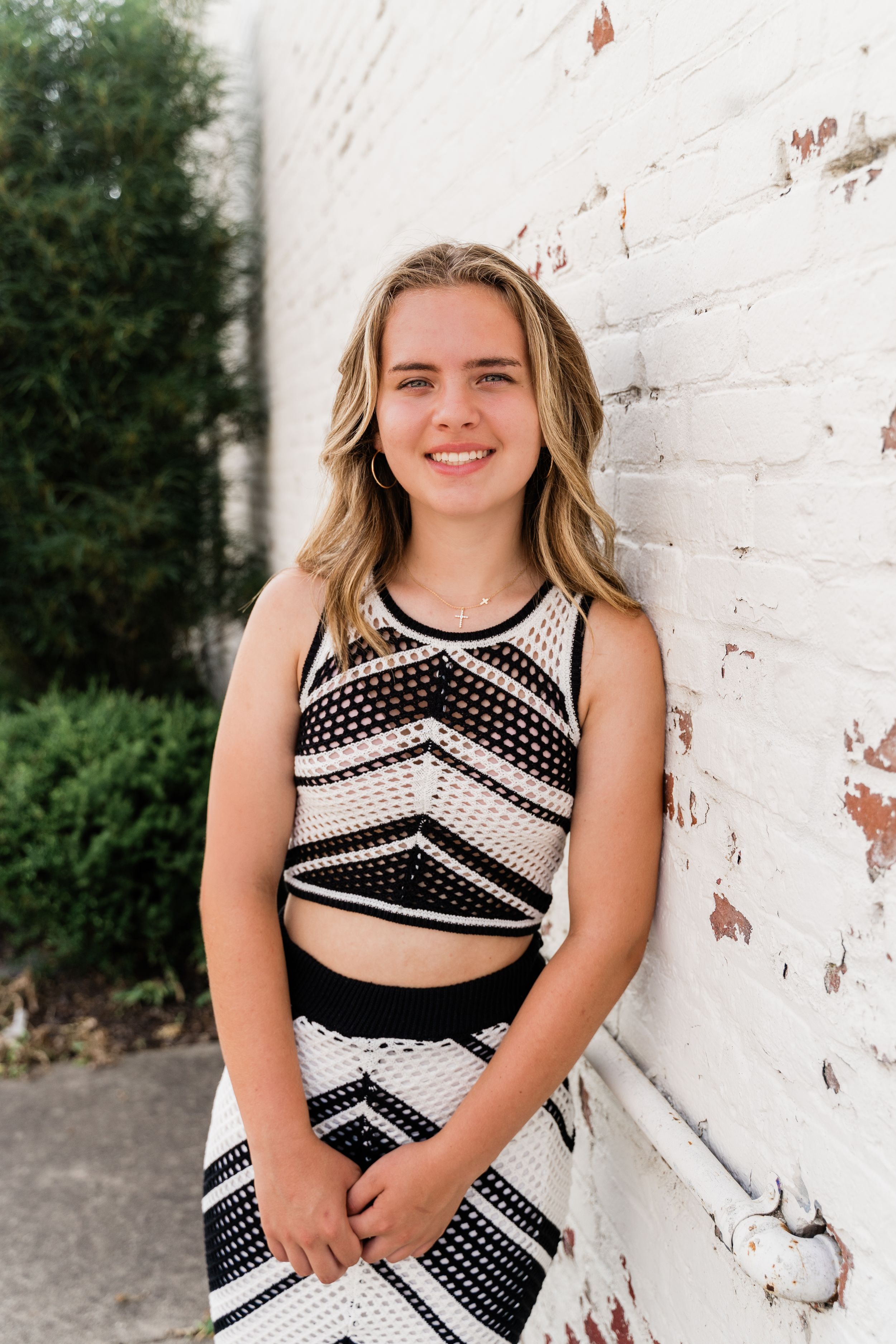 A cheerleader in a black and white uniform poses against a white brick wall in a series of photos.