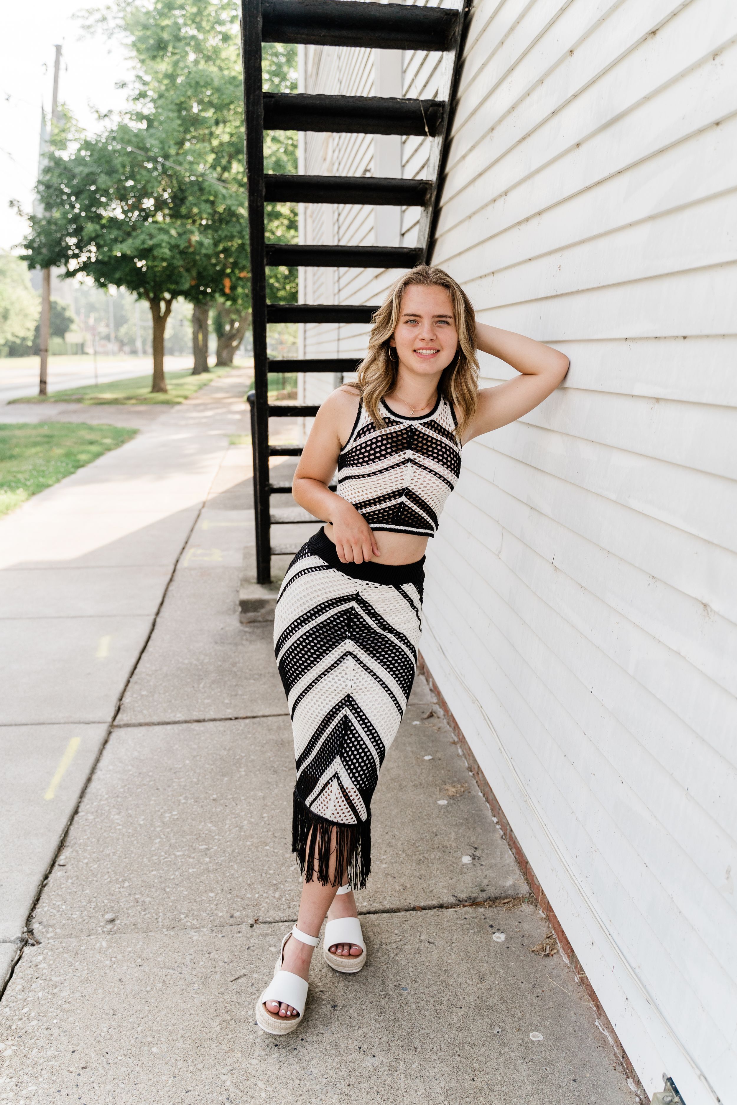A series of photos showing someone in a black and white patterned dress posing against a white wall outdoors.
