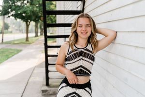 A person in a black and white patterned dress poses against a white wall in multiple casual outdoor shots.