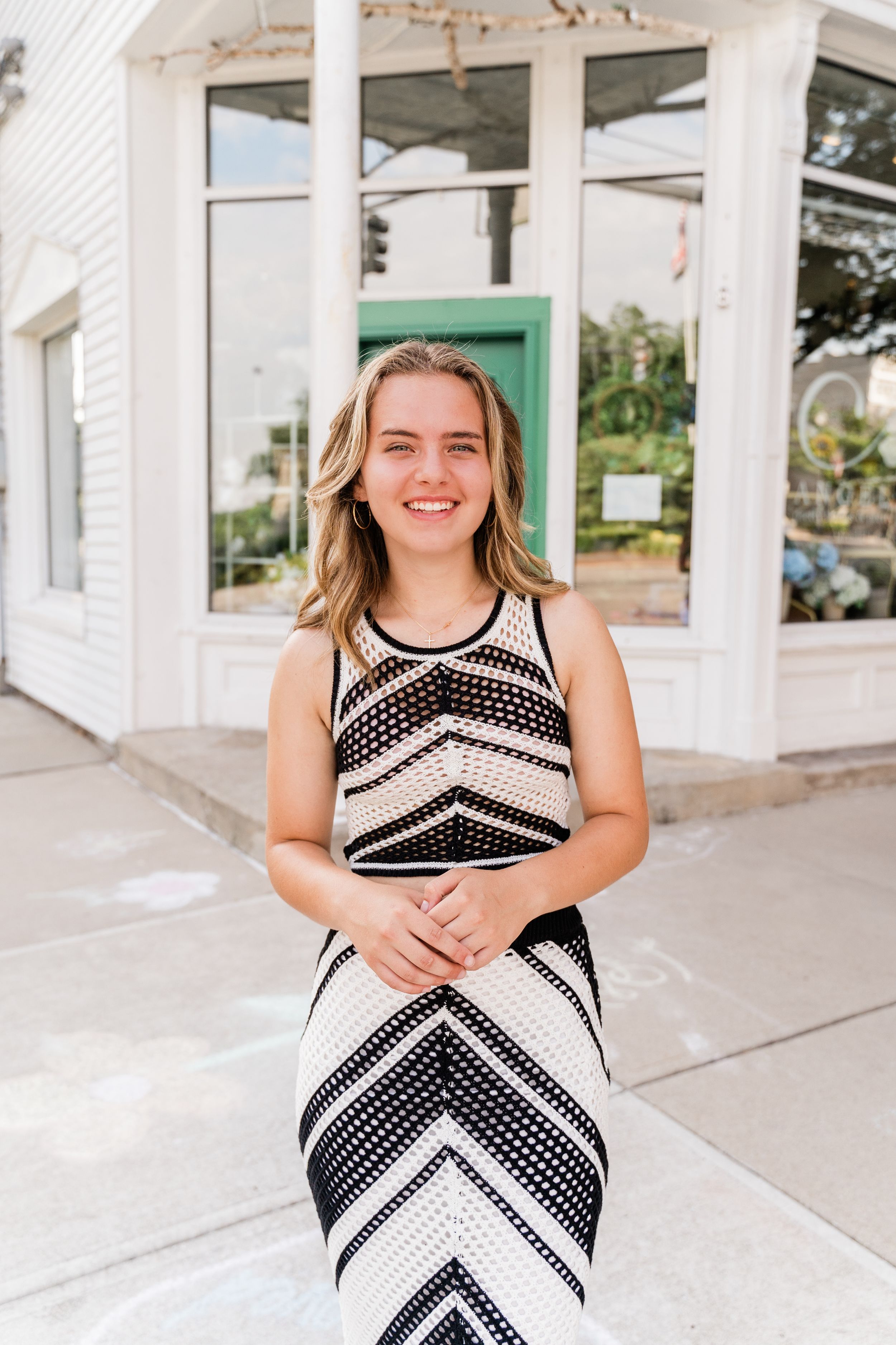 Person wearing a black and white chevron pattern dress stands smiling on a porch with a green door in the background.