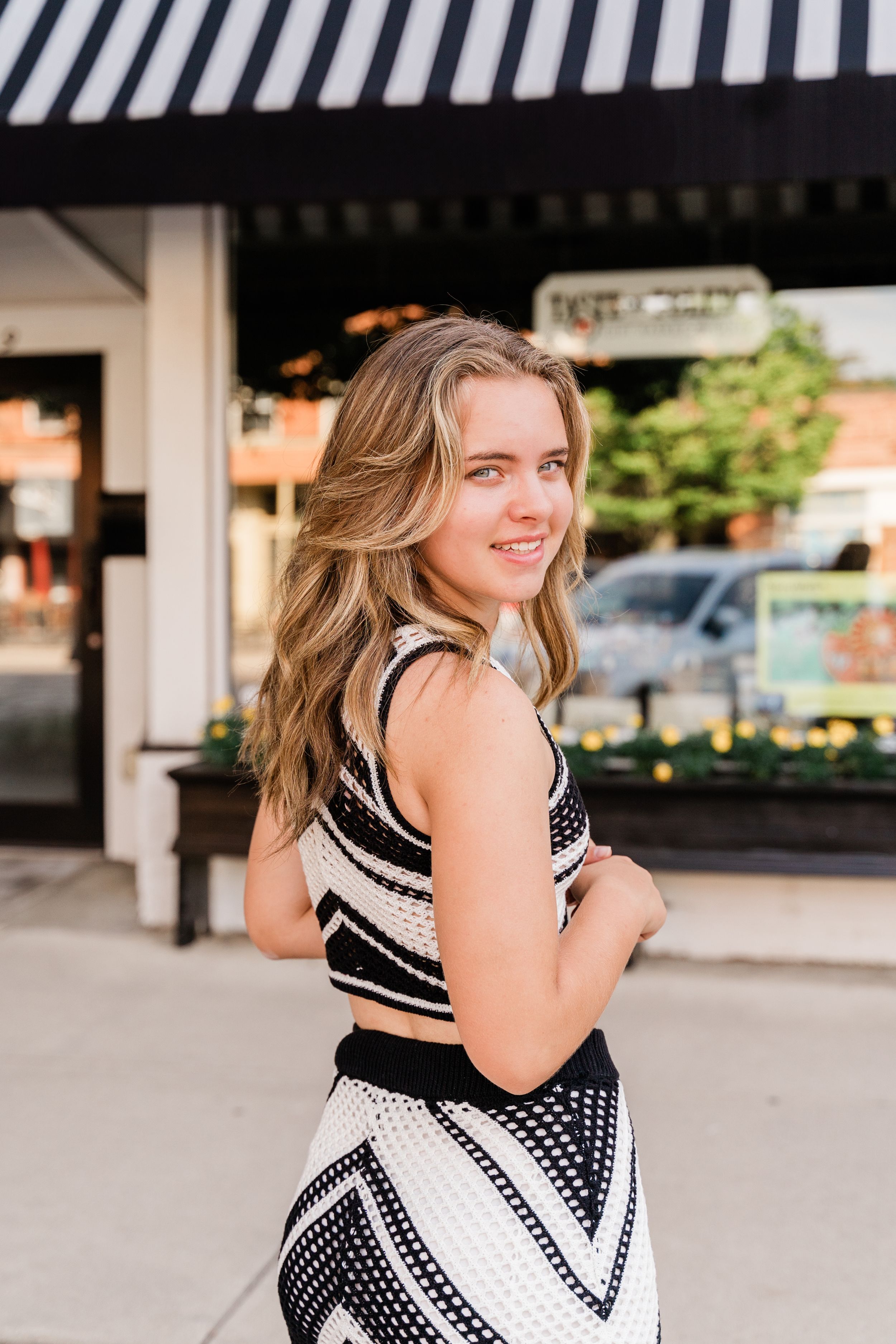 Woman in black and white polka dot dress poses in front of outdoor storefront in series of candid shots.