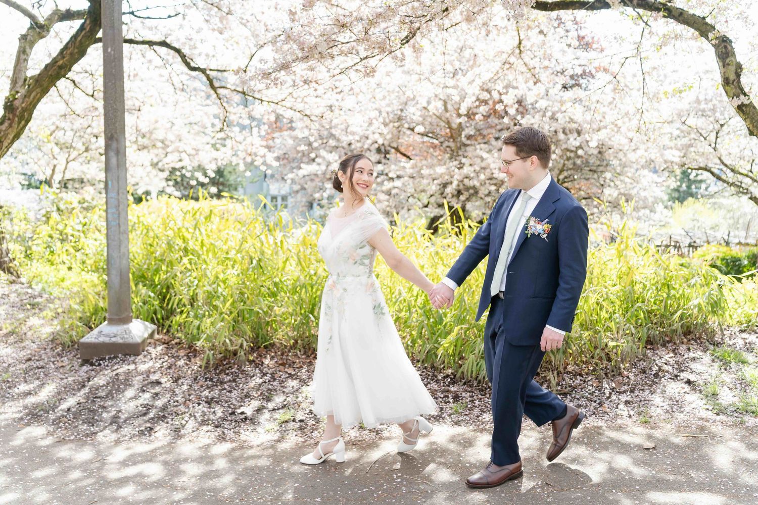 A couple shares a romantic moment under blooming cherry blossom trees with a vintage lamp post in the background.