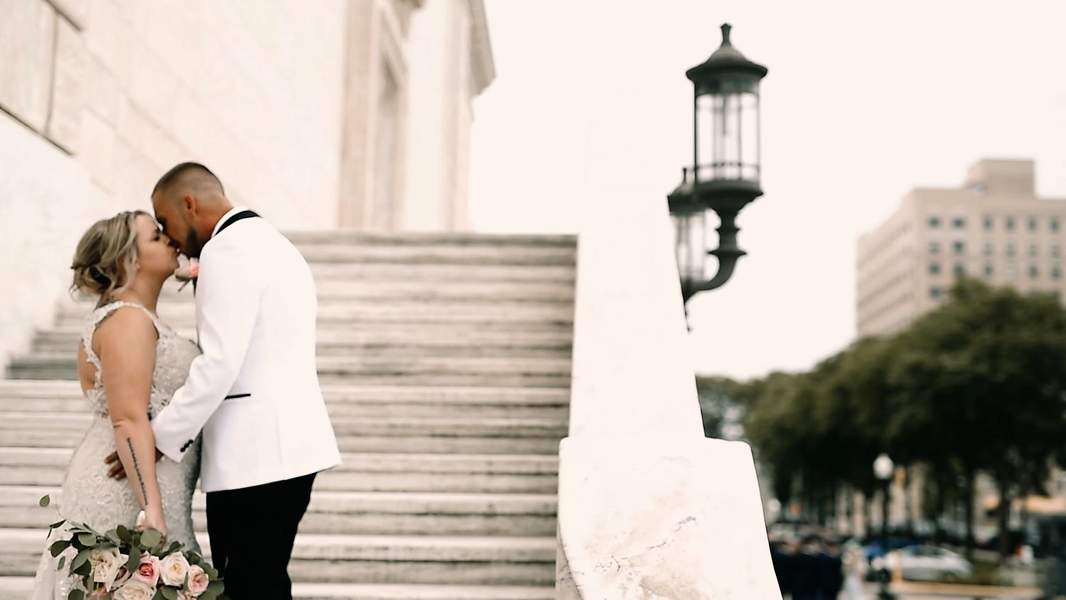 A wedding couple embraces on marble steps outside a grand building with columns during their special day.