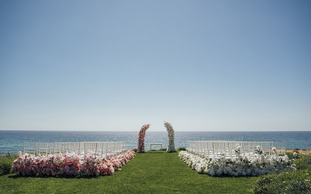 Panoramic view of white beach chairs lined up along a grassy oceanfront overlooking the blue sea and horizon.