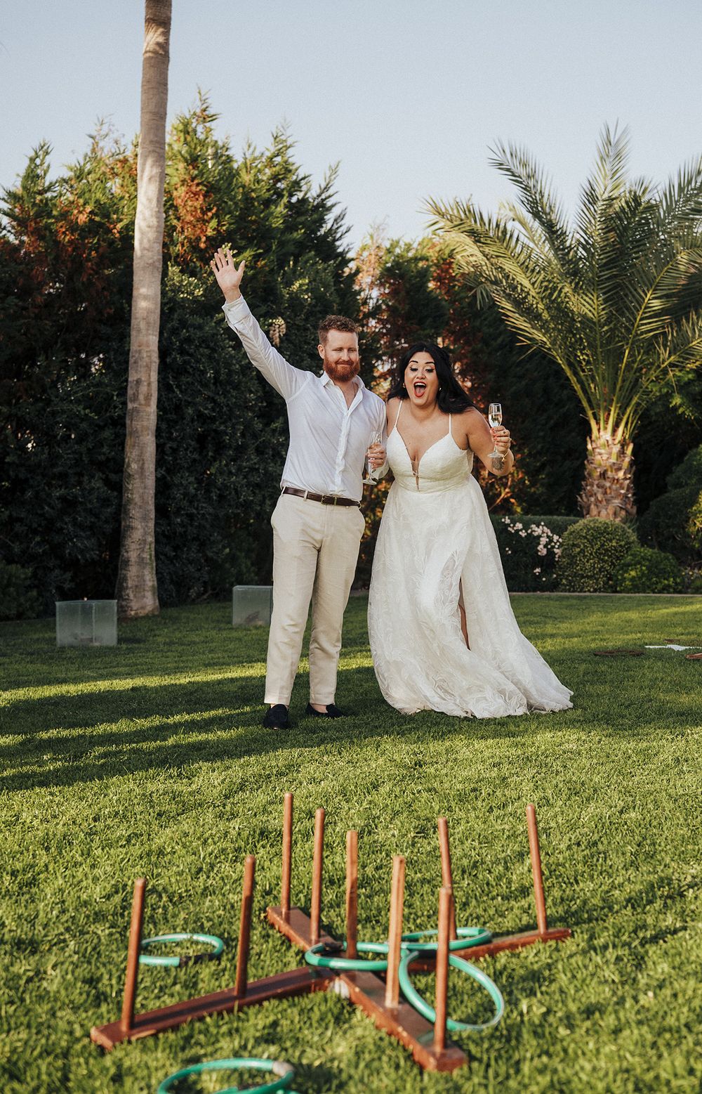 A couple in wedding attire playing lawn games with colorful rings and wooden stakes on a grassy outdoor area.