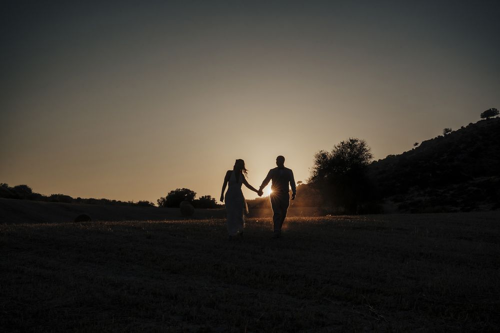 Silhouettes of a couple walking together at sunset against a dramatic dusky sky.