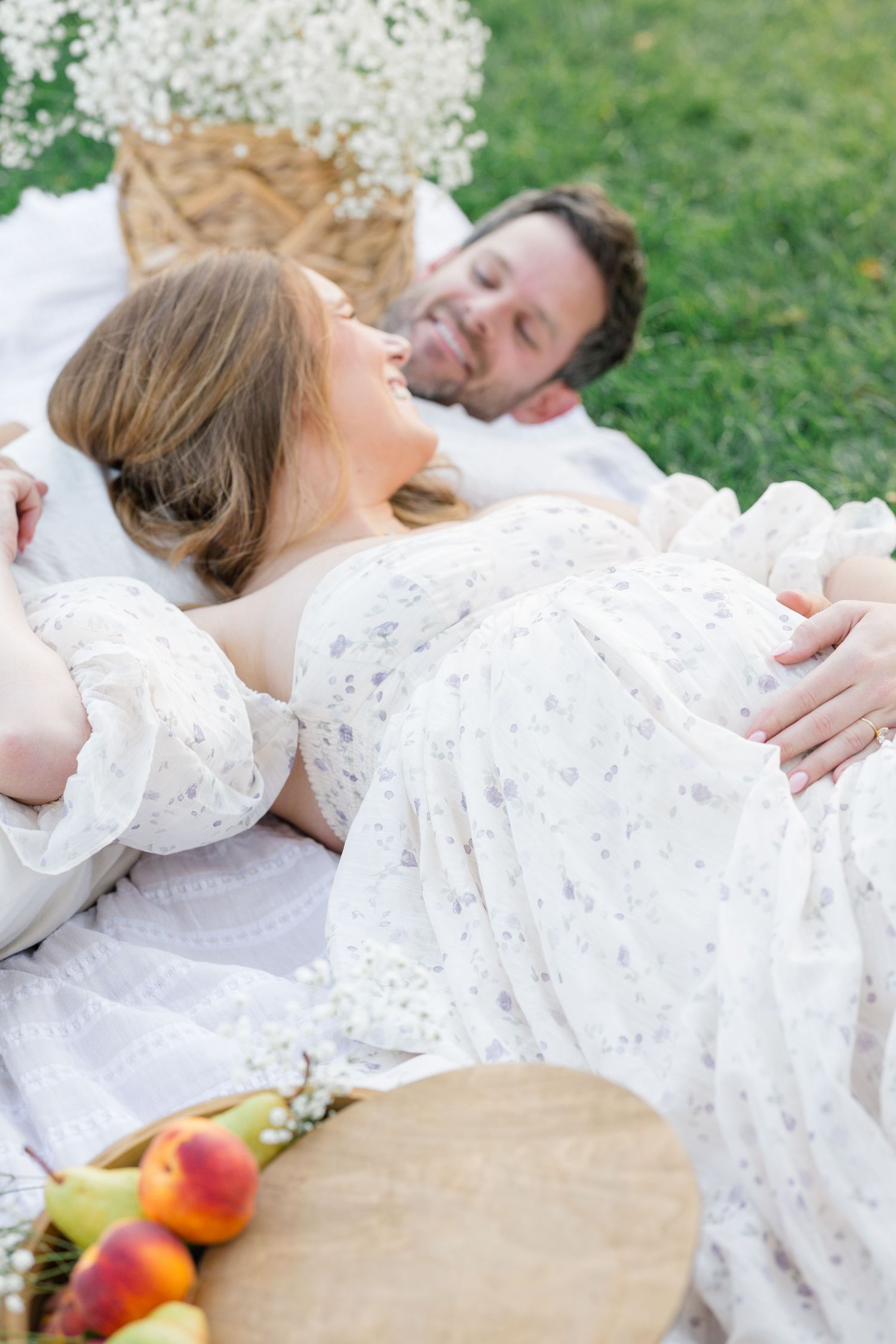 An expecting couple on picnic blanket surrounded by glowing sunlight, fruit, and delicate floral during a maternity session in Pittsburgh.