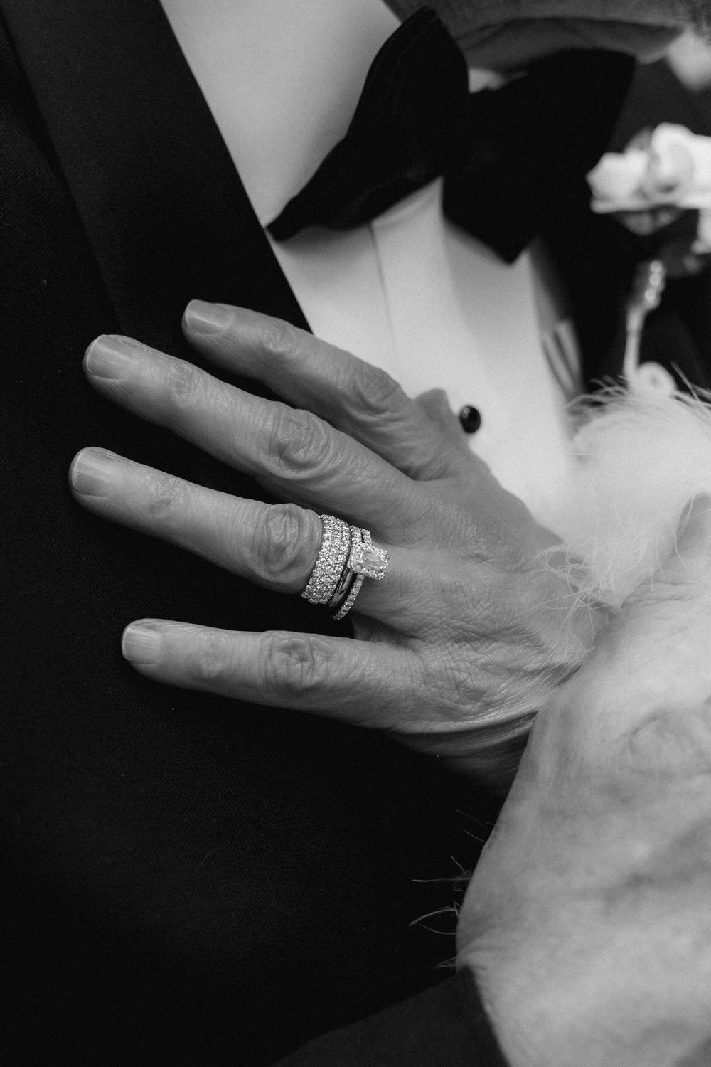 Close-up black and white photo showing hands with wedding rings against white fabric background.