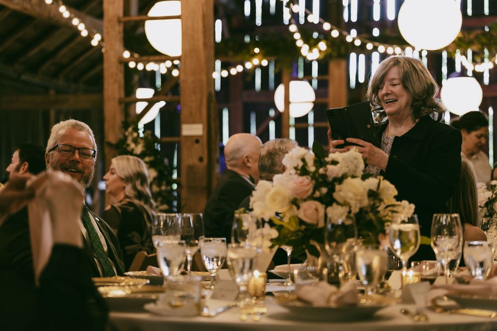Guests enjoy a festive dinner celebration in a rustic barn venue decorated with string lights and floral centerpieces.