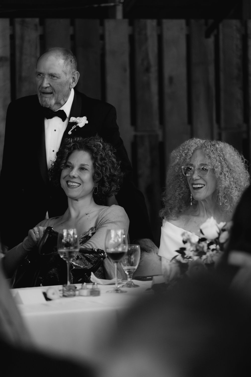 Black and white photo of guests laughing and smiling at an elegant formal dinner reception.